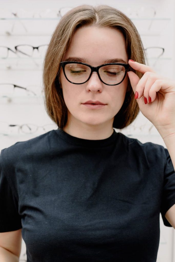 Young woman in optical store trying on modern eyewear, considering options.